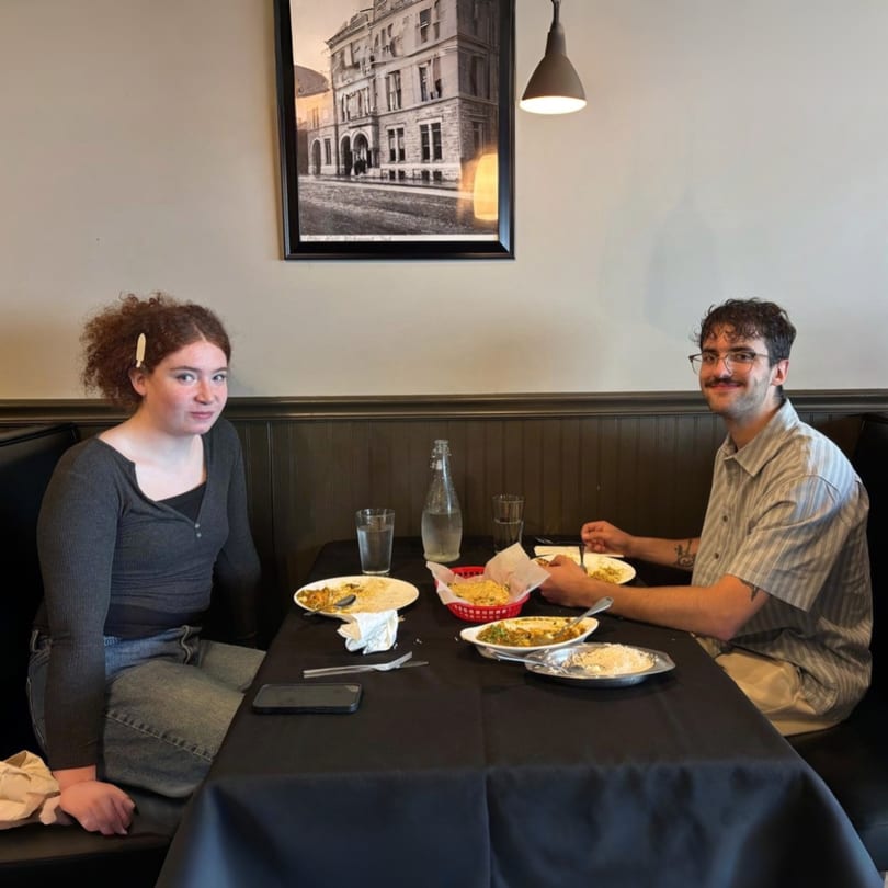 Two young people enjoying a meal together at a restaurant table with Indian food.