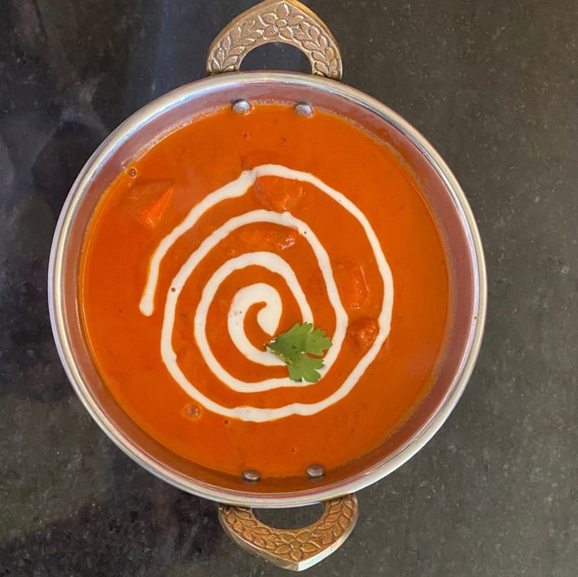 Overhead view of butter chicken in a silver bowl, garnished with cream swirl and cilantro.