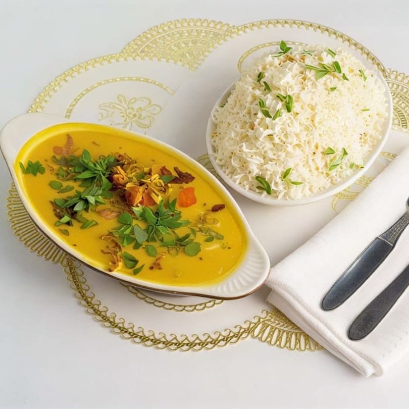 Yellow lentil dal with herbs and fried onions, served with white rice and cutlery.